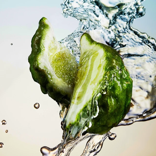 Two halves of a vibrant green citrus fruit, glistening with water droplets, are suspended in a dynamic splash against a gradient background.