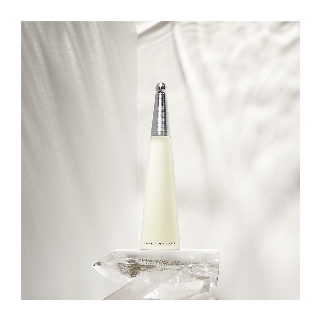 Elegant photo of Issey Miyake perfume bottle on a quartz crystal, featuring a minimalist white background and subtle light play.