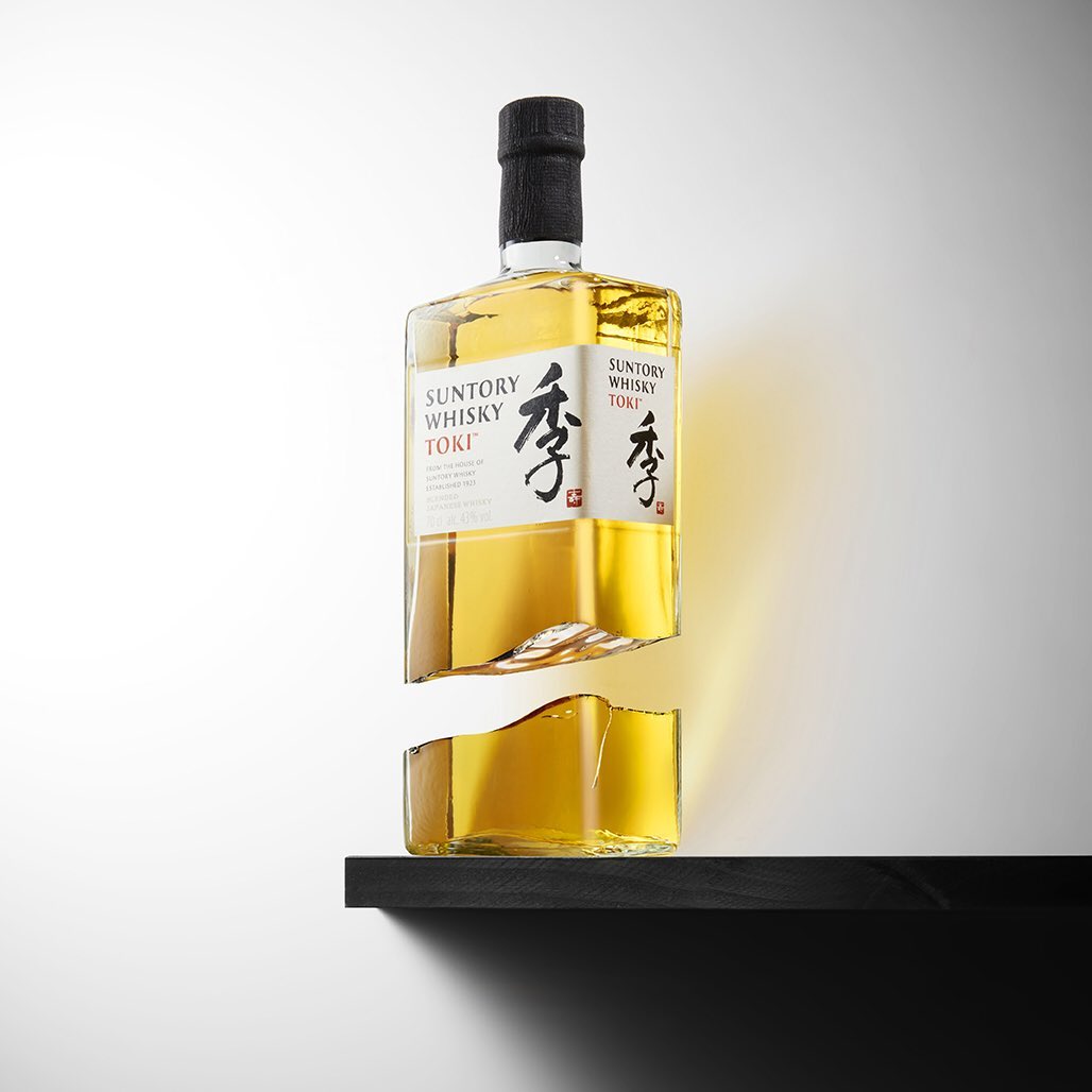 Studio shot of a Suntory Whisky Toki bottle with a broken effect, featuring golden liquor on a black shelf against a white background.