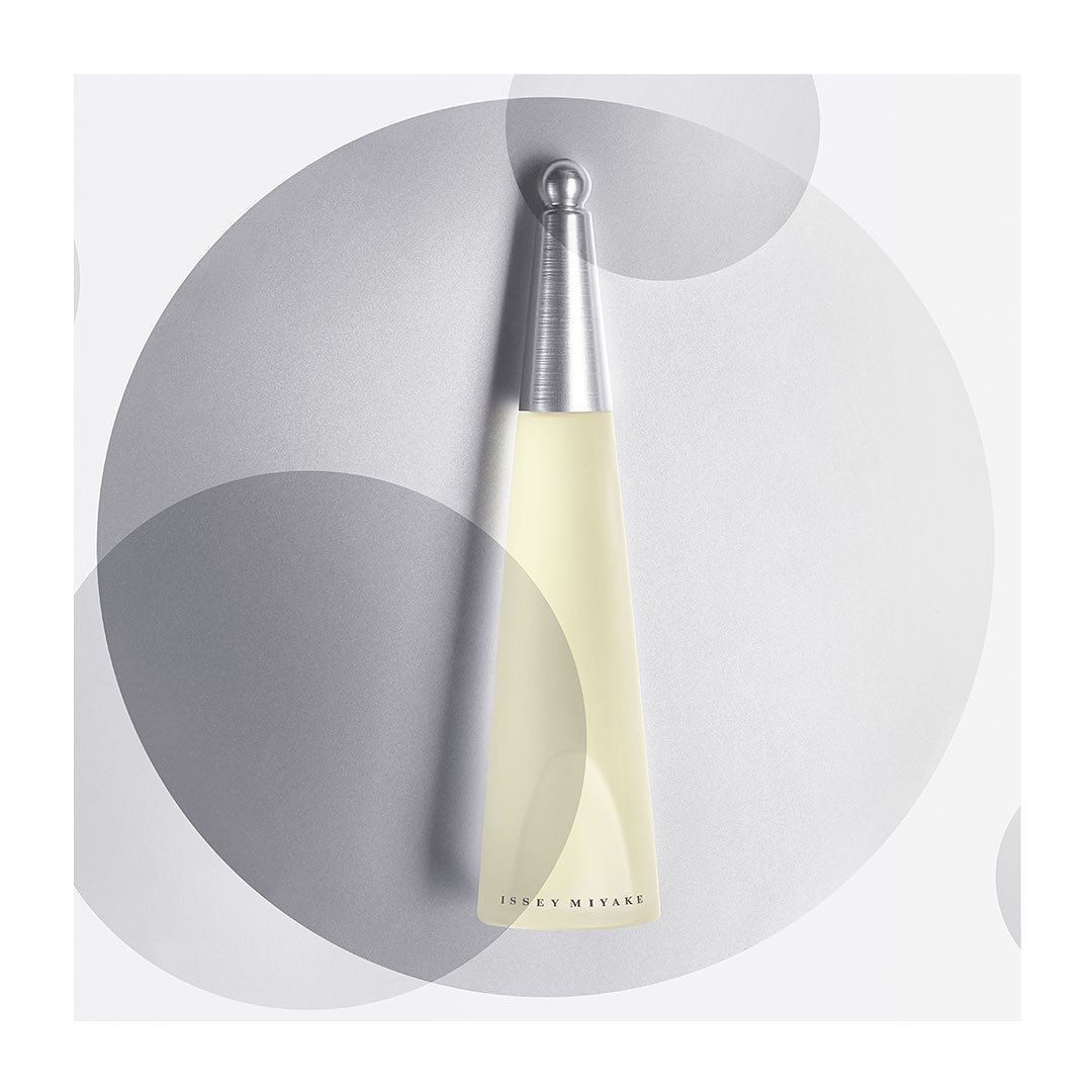 Angled presentation of an Issey Miyake perfume bottle with a silver cap and a light yellow liquid set against a gray, bokeh-dot backdrop.