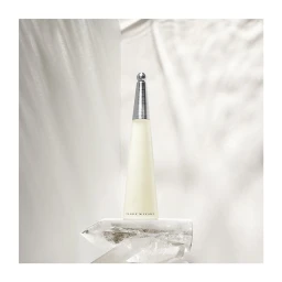 Tall cone perfume bottle with silver cap resting on a crystal quartz prism against draped white fabric