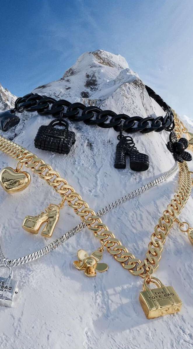 Jewelry charms necklaces featuring miniature handbags and high-heeled shoes on snowy mountain backdrop, fashion product shot.
