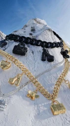 Layered charm necklaces with miniature bag and shoe pendants resting against a snowy mountain peak under a clear blue sky