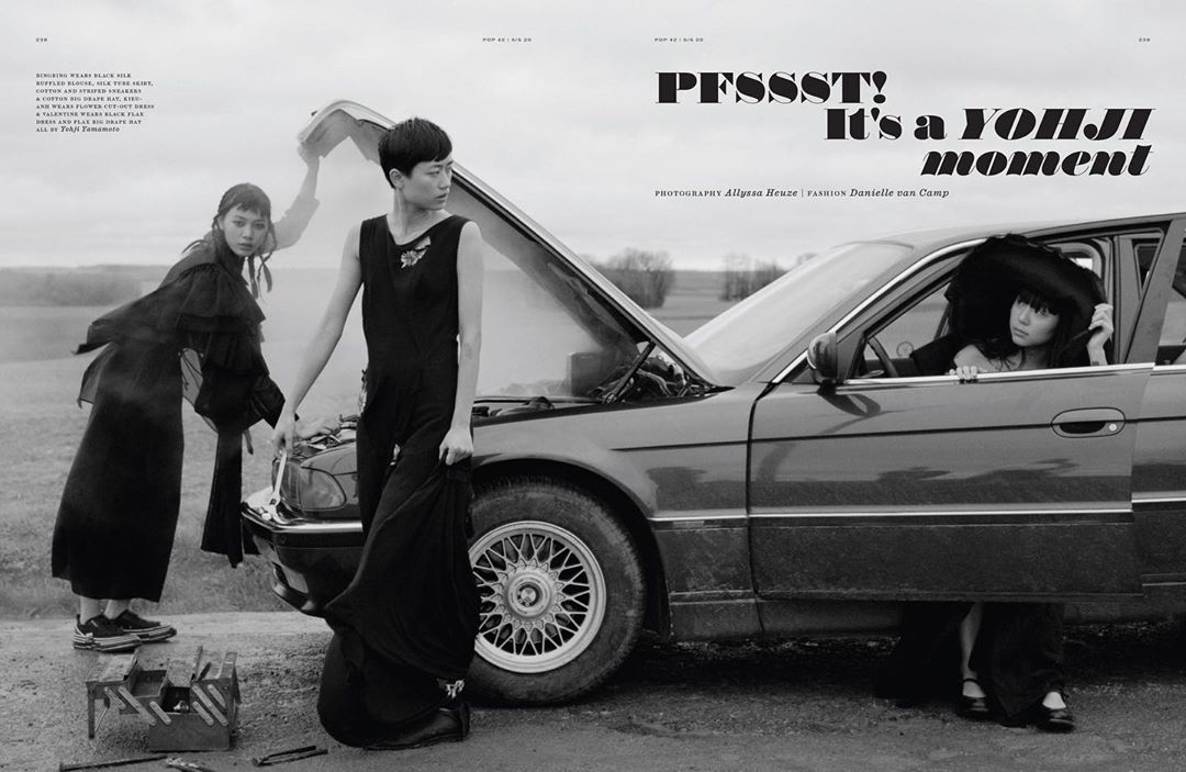 Three women in black dresses stand by a vintage car with its hood open in a rural setting. Fashion editorial photography.