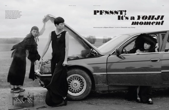 Three women in black dresses stand by a vintage car with its hood open in a rural setting. Fashion editorial photography.
