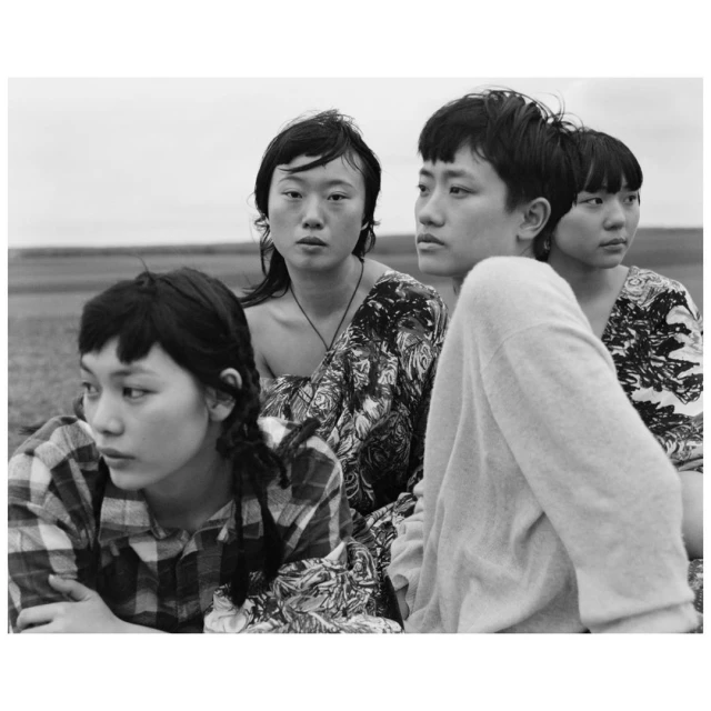 Black and white portrait of four young Asian women in an outdoor setting with a blurred background, showcasing natural light and fashion.