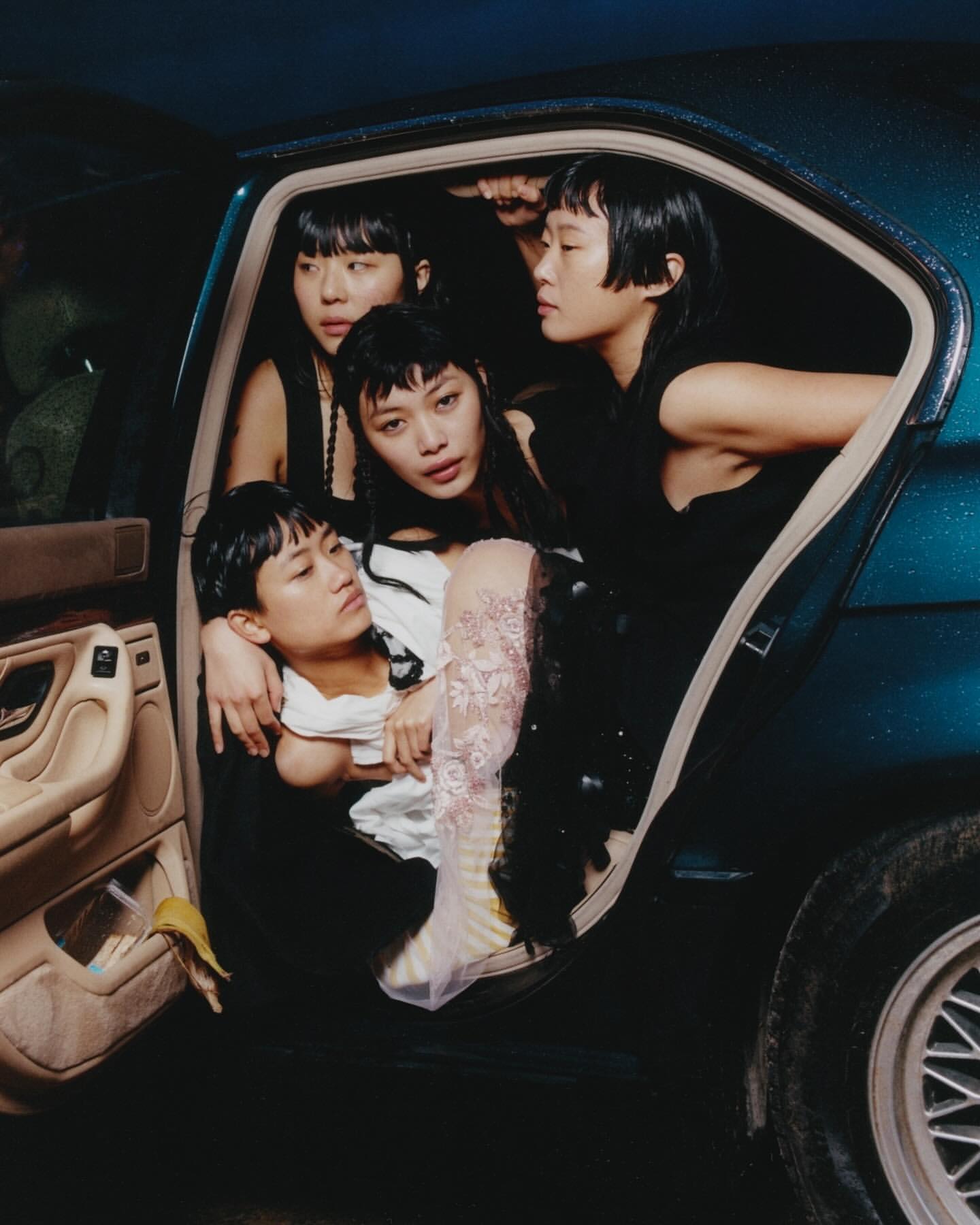 Four young Asian women huddle in the backseat of a blue car, creating a striking and intimate group portrait. Fashion, beauty shot.