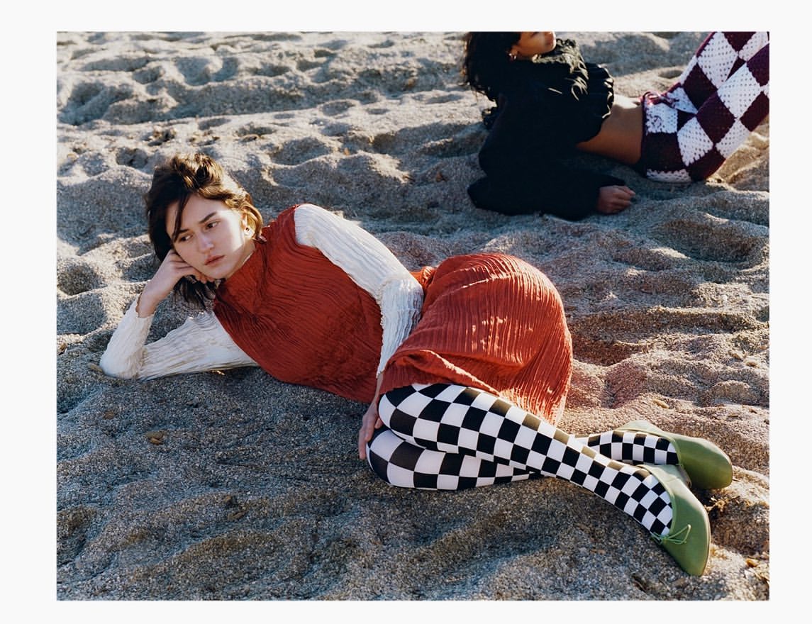 Two women lying on a sandy beach wearing textured patterned clothing and colorful tights