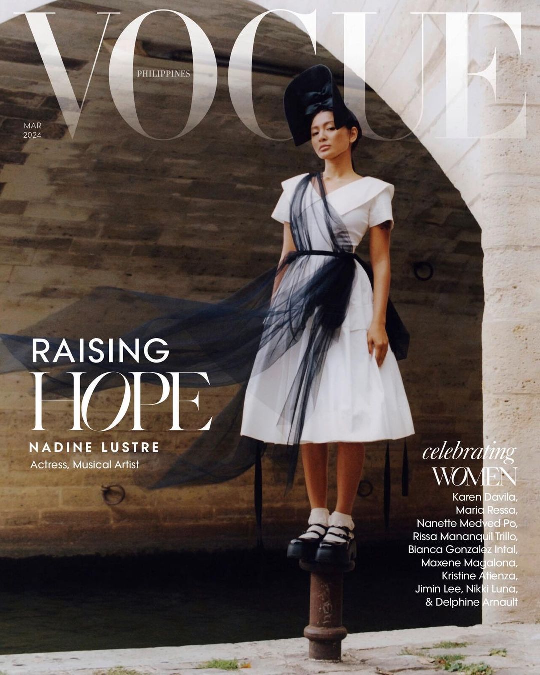 Vogue Philippines cover with Nadine Lustre in a white dress and black hat standing on a pole, featuring stone arches in the background.