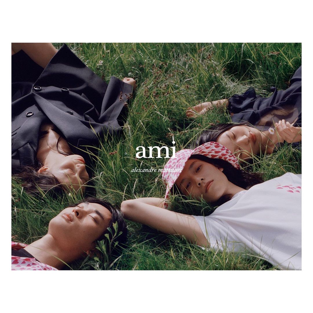 Four young adults rest on lush green grass outdoors, posing for a fashion editorial, showcasing youthful style and natural setting.