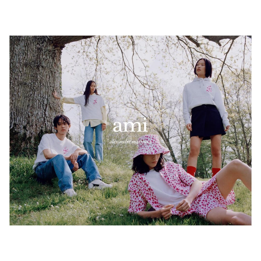 Group of four young adults wearing casual clothes outdoors on green grass near a tree for a fashion brand campaign.