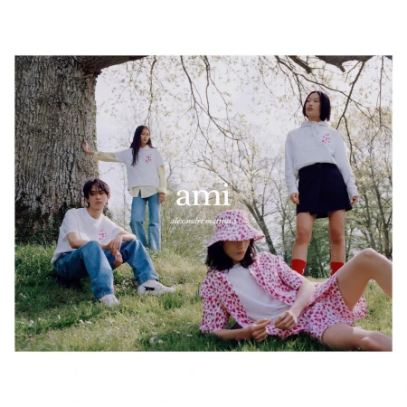Group of four young adults wearing casual clothes outdoors on green grass near a tree for a fashion brand campaign.