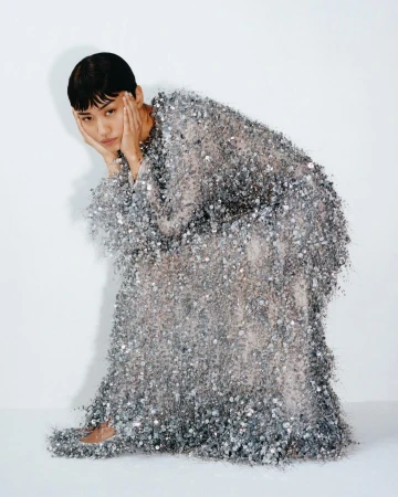 Model with short dark hair in a textured silver embellished gown posing against a plain white background.
