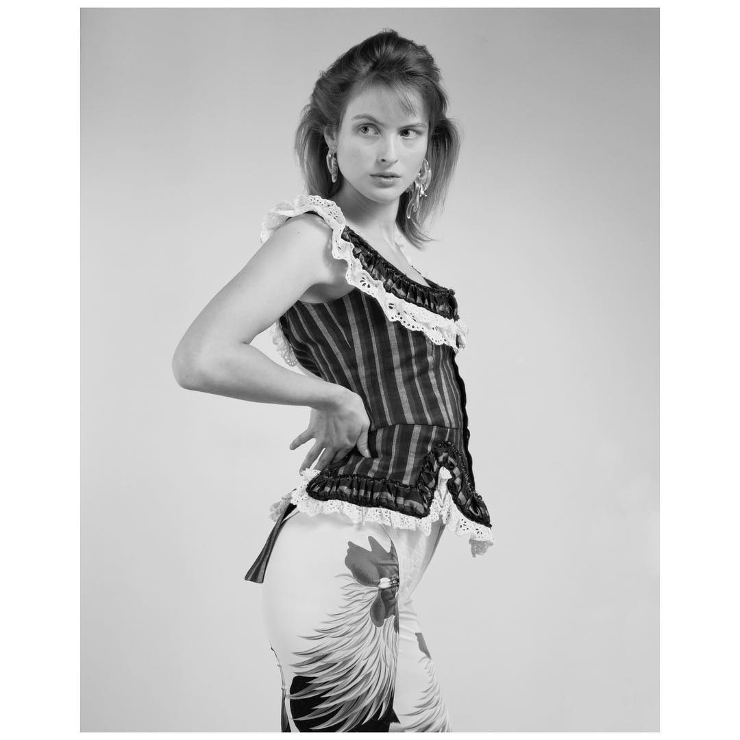 Black and white portrait of a woman in a striped top and floral pants, posing with hand on her hip against a neutral background.
