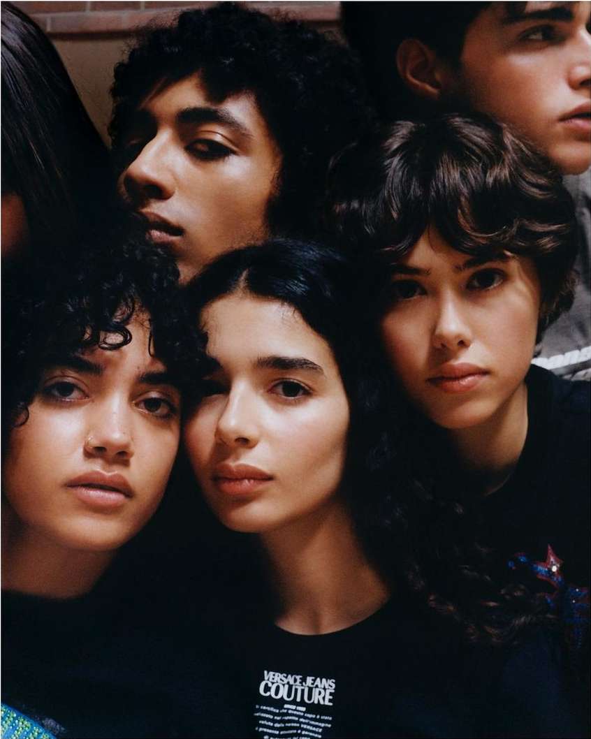 Group of young adults in a close-up portrait. The group of people have dark hair, light skin, and face forward. Some of the individuals wear black shirts.