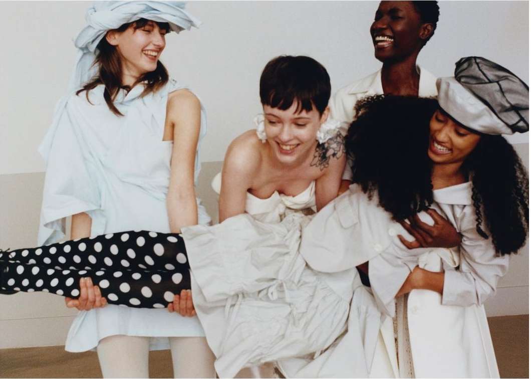 Group of five diverse women in a studio setting, smiling and laughing while one woman is lifted by two other women.