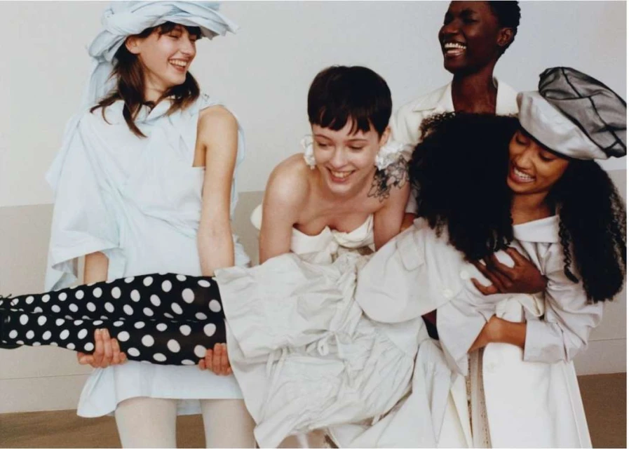 Group of five diverse women in a studio setting, smiling and laughing while one woman is lifted by two other women.