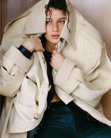 Close-up portrait of a woman wearing an oversized cream-colored coat pulled over her head, photographed by Allyssa Heuze