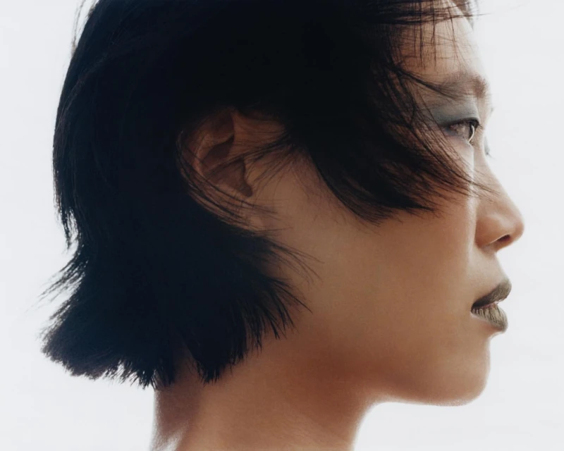 Profile portrait of adult woman with dark choppy hair and olive lipstick against bright white. Beauty and fashion portrait.
