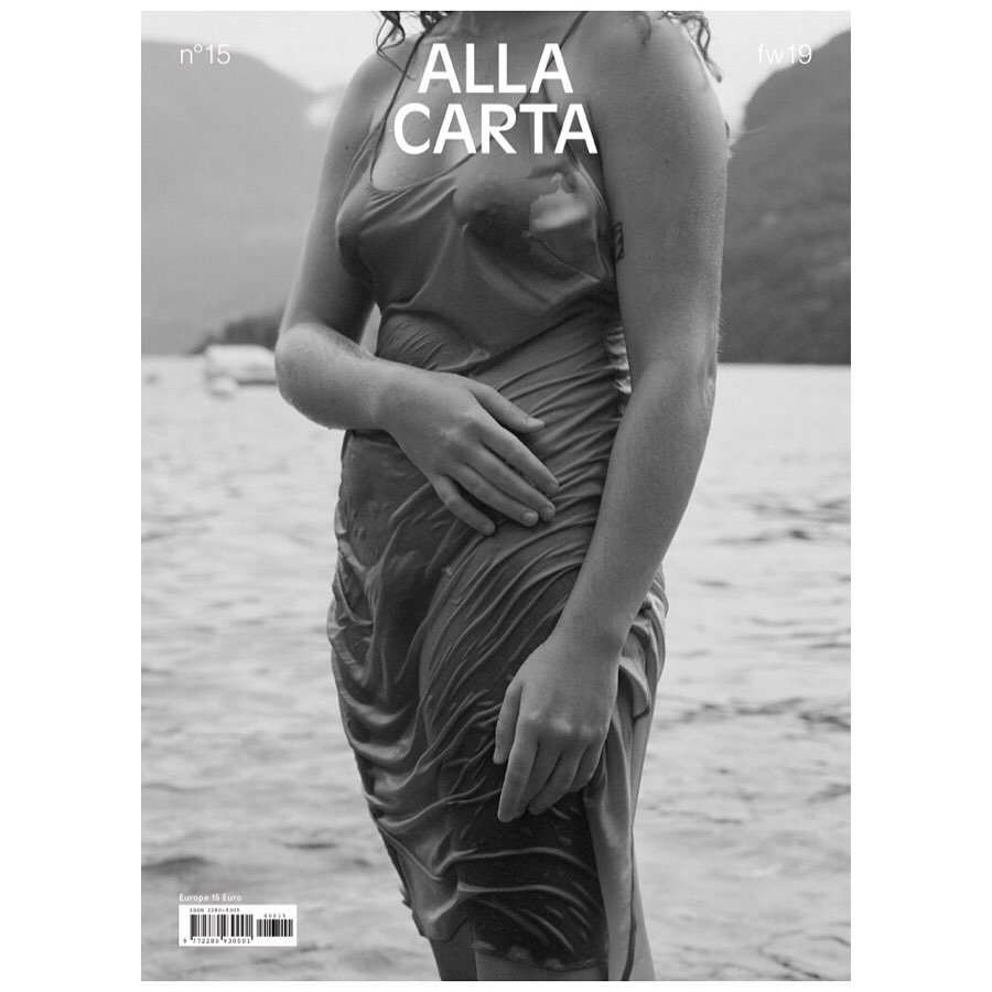 Black and white magazine cover featuring a model in a wet dress standing in water against a blurred background of mountains and trees.