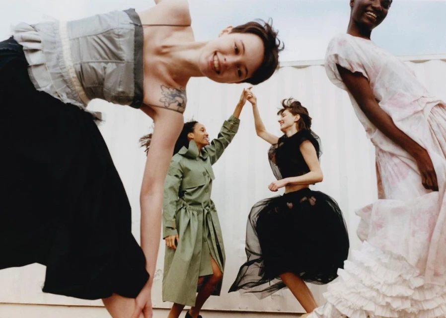 Fashion photo featuring five female models in dresses and a trench coat striking poses against a plain white backdrop, showcasing various styles.