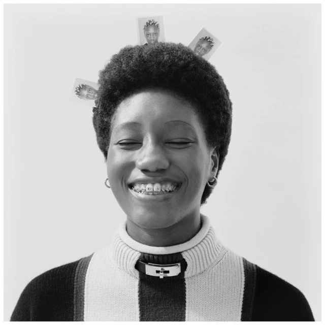 Portrait of a Black woman with a bright smile and braces, wearing a striped turtleneck sweater, with photos around her afro hairstyle.