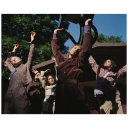 Group of people in stylish autumn apparel posing outdoors with arms raised up against a blue sky.