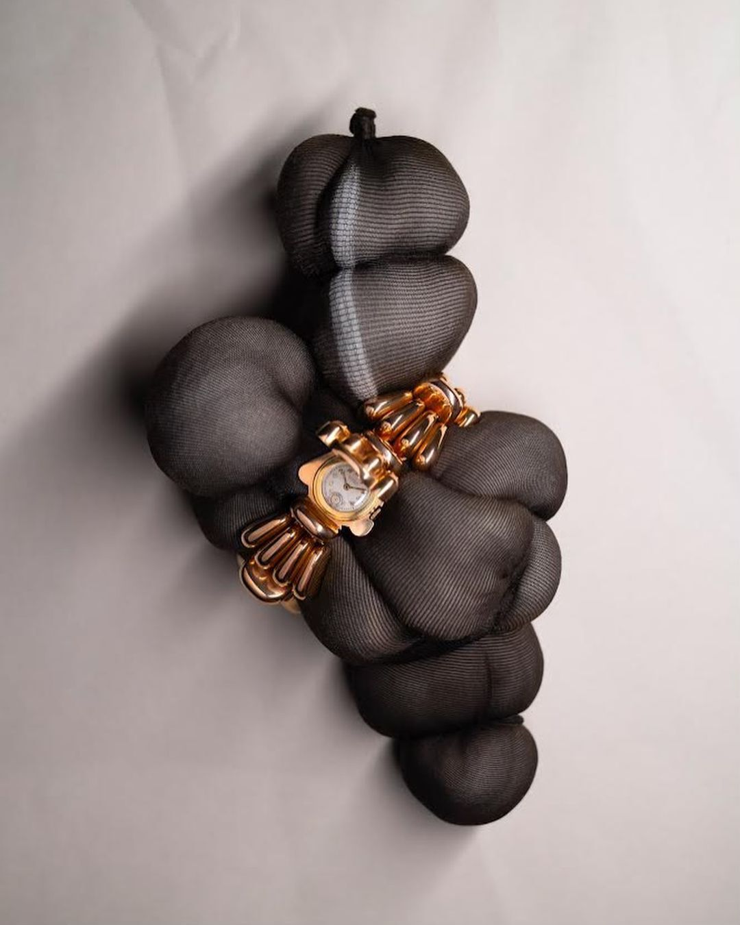 Gold-tone bracelet watch with decorative sculptural band, showcased atop dark draped fabric with neutral backdrop, elegant timekeeping.