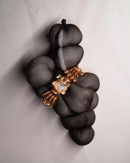 Gold-tone bracelet watch with decorative sculptural band, showcased atop dark draped fabric with neutral backdrop, elegant timekeeping.