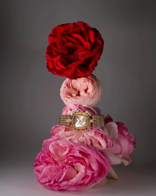 Gold wristwatch presented atop stacked pink and red roses against a neutral background in an indoor product photography setting.