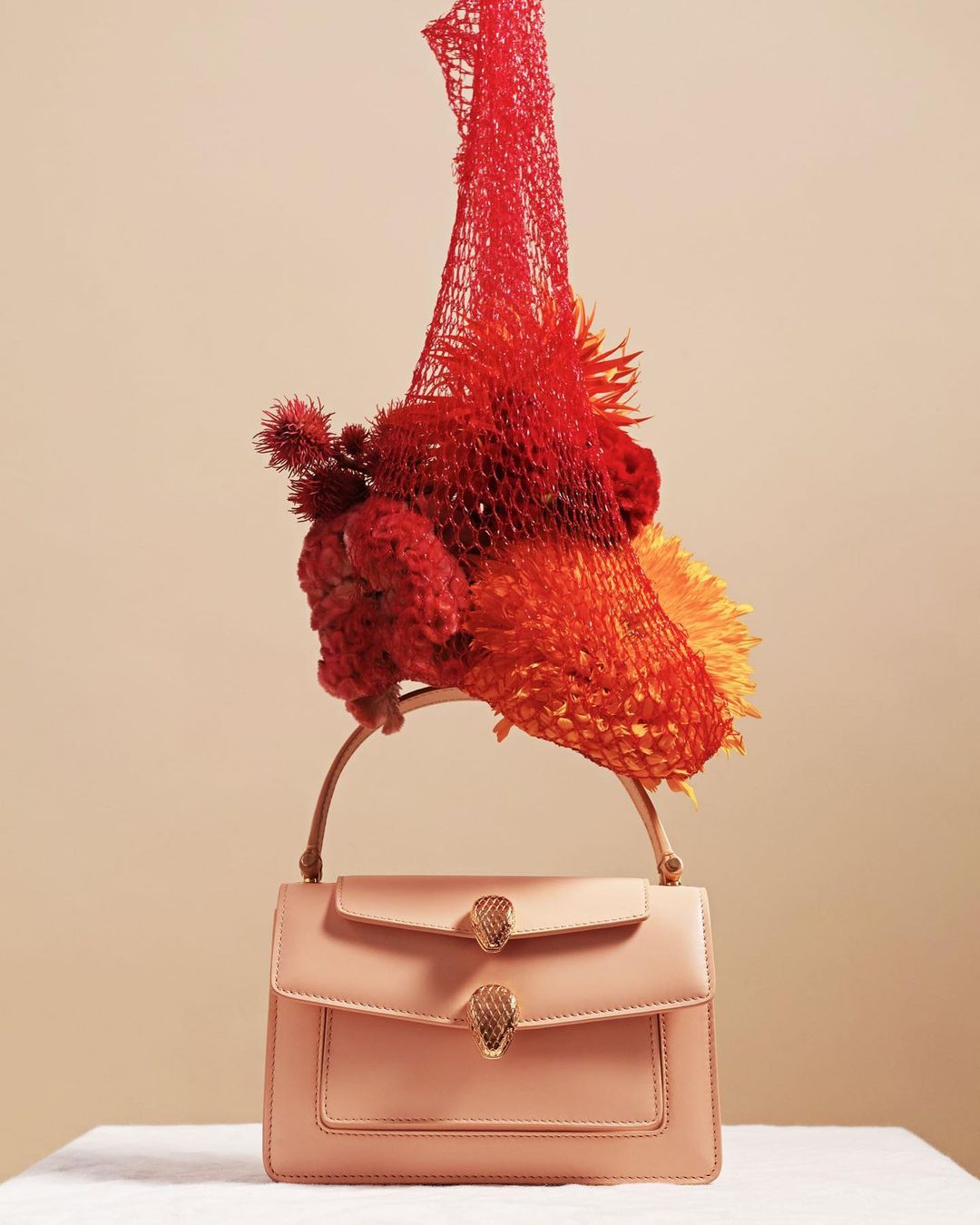 Elegant purse with an artistic floral display on a white platform against a neutral background, creating a fashion-forward composition.