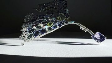Close-up of a luxury statement headpiece featuring ornate silver metalwork and assorted, faceted gemstones on a white surface.
