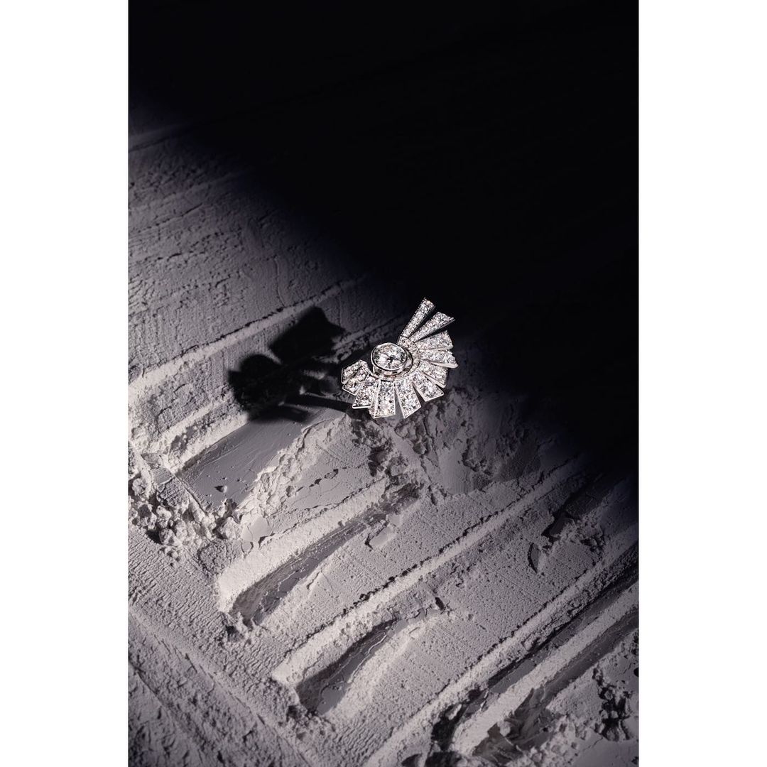 Close-up of a diamond brooch on a powder surface, with a dark background creating strong contrast and highlighting the jewelry's detail.