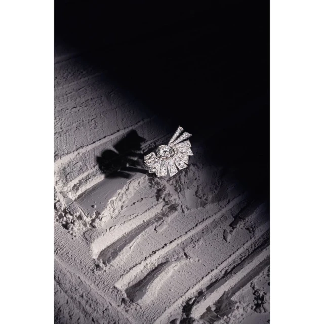 Close-up of a diamond brooch on a powder surface, with a dark background creating strong contrast and highlighting the jewelry's detail.