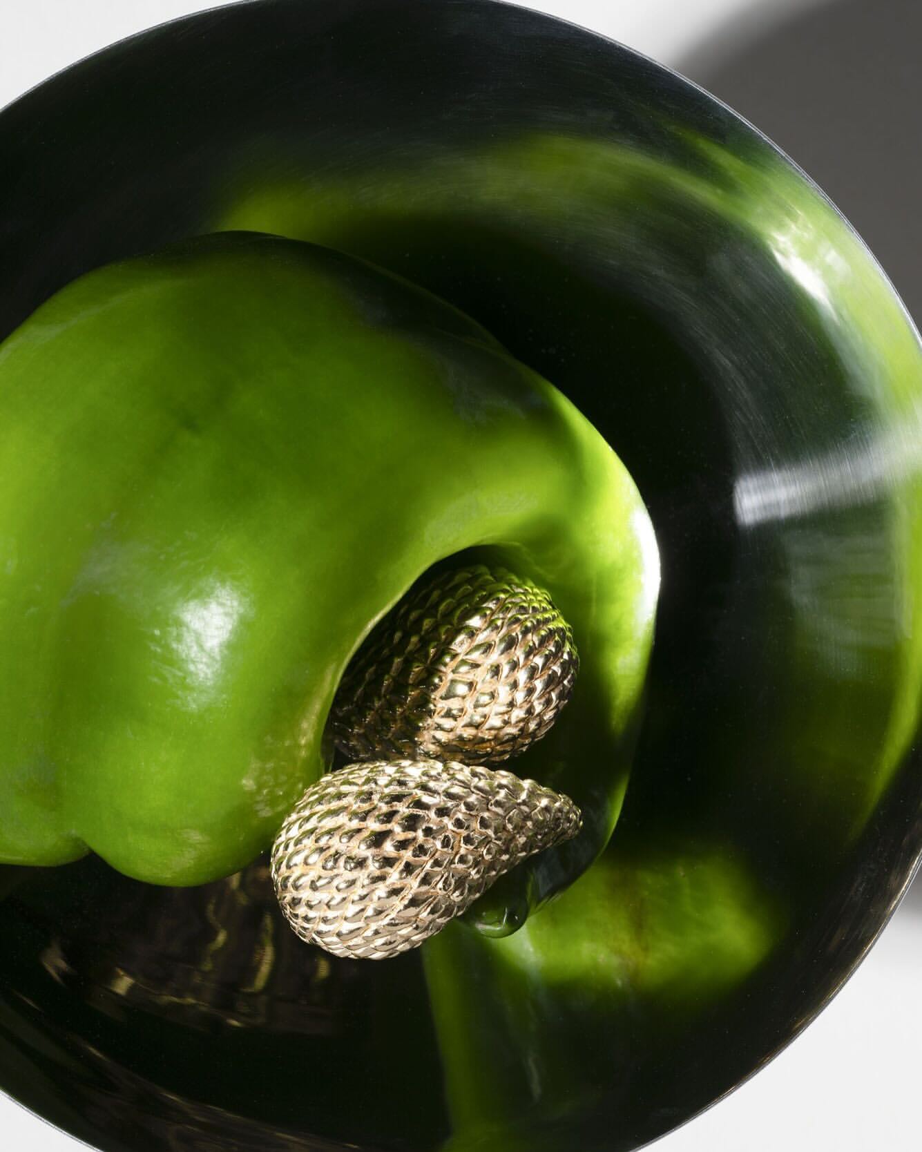 Close-up studio shot of a green bell pepper with metallic gold stamens in the center, highlighting vibrant color and texture.