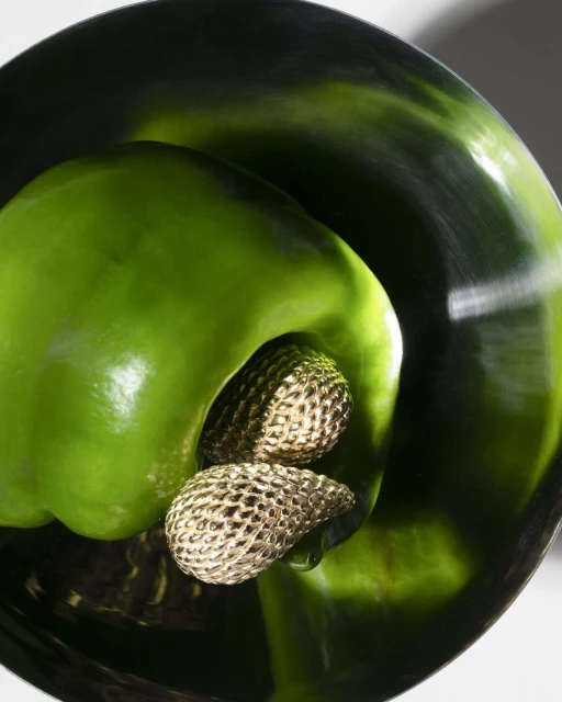 Close-up studio shot of a green bell pepper with metallic gold stamens in the center, highlighting vibrant color and texture.