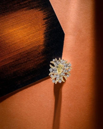 Close-up of an ornate gold ring with diamonds and a yellow gemstone set against a copper-colored surface with a dark painted corner accent.