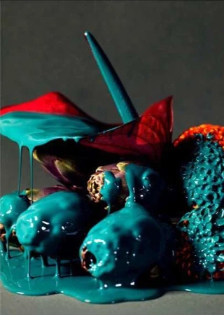 Still life of fruit and anthurium flowers covered in teal paint creating a vibrant and surreal visual, set against a grey backdrop.