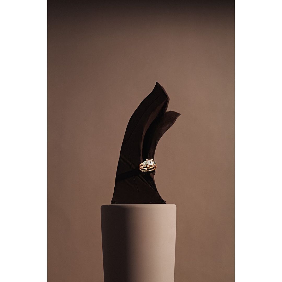 Still life product shot: An elegant wedding ring set displayed on a modern sculpture on a matte pillar against a tan backdrop.