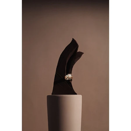 Still life product shot: An elegant wedding ring set displayed on a modern sculpture on a matte pillar against a tan backdrop.