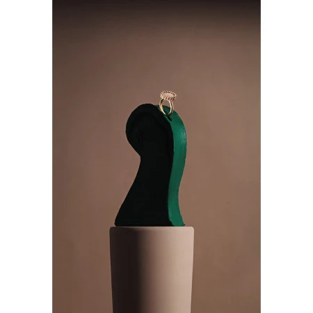 Gold ring resting on top of a dark green abstract sculptural bust against a warm taupe studio background.