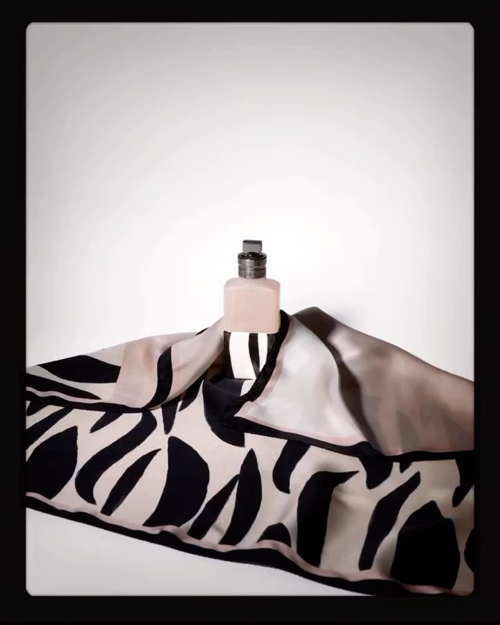 Perfume bottle presented on black and white patterned scarf against white backdrop, product shot for fashion or beauty brand.