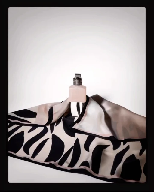 Perfume bottle presented on black and white patterned scarf against white backdrop, product shot for fashion or beauty brand.