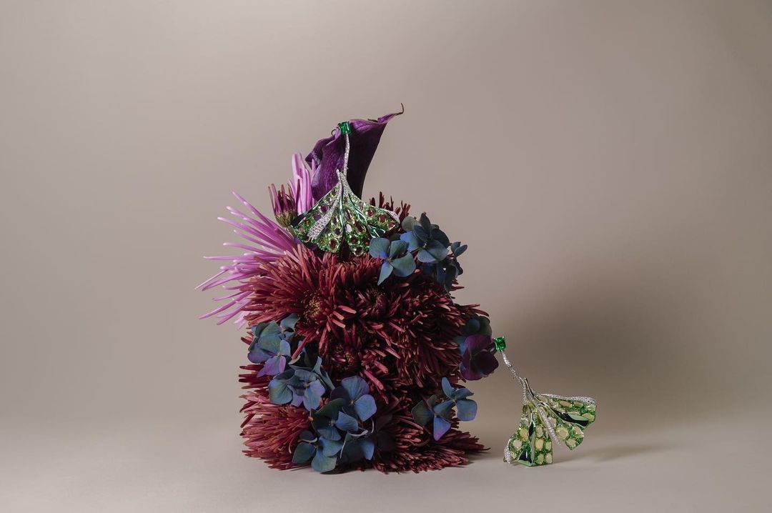 Close-up of purple and blue flowers arranged with ornate metal earrings. The still life composition has a studio aesthetic.