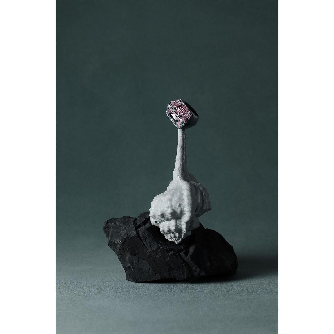 Close-up of a gemstone ring displayed on top of a grey sculpted base atop a black rock against a grey-green backdrop. Jewelry concept.