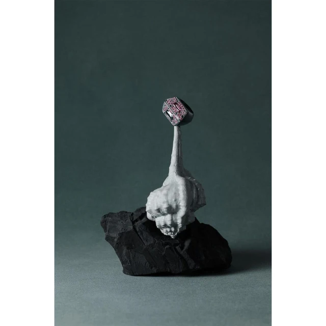 Close-up of a gemstone ring displayed on top of a grey sculpted base atop a black rock against a grey-green backdrop. Jewelry concept.