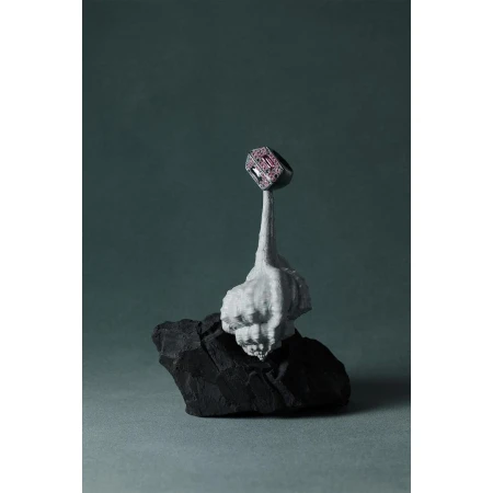 Close-up of a gemstone ring displayed on top of a grey sculpted base atop a black rock against a grey-green backdrop. Jewelry concept.