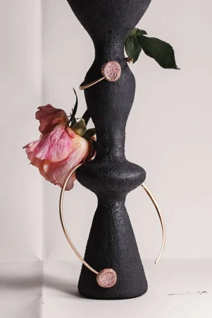 Black textured vase with gold jewelry and pink rose. Modern studio shot, emphasizing texture and color contrast. Minimalist composition.
