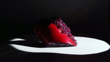 Striking studio shot of a red high-heel shoe adorned with vibrant pink crystals, illuminated by a dramatic spotlight.