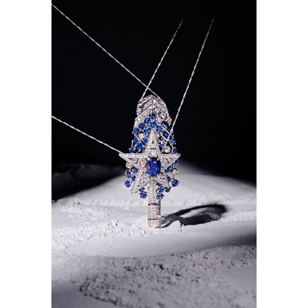 Necklace with blue gemstones in star and drop shapes on a white reflective surface with a dark grey background, studio shot.